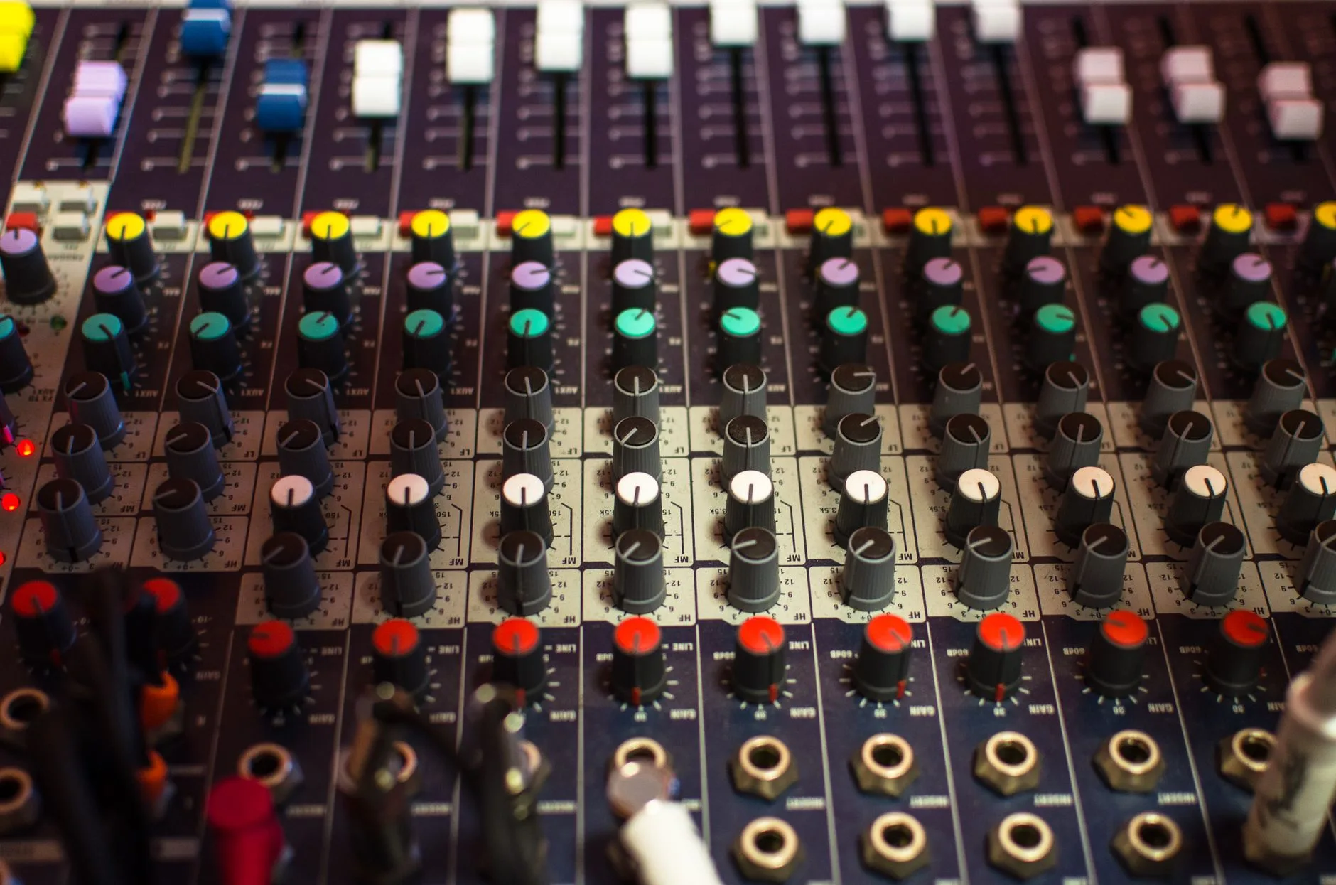 Close-up of an audio mixing console with colorful faders and knobs in a dubbing studio