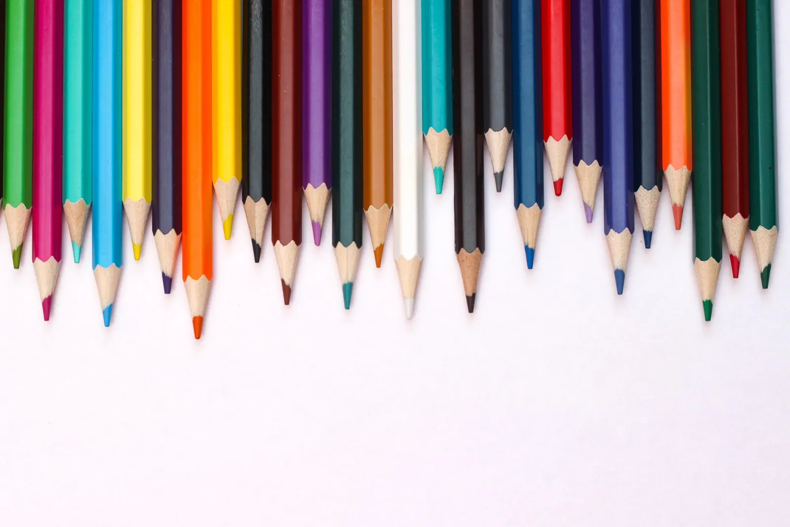 Top view of multicolored, sharpened pencils neatly arranged with copy space on a white background.