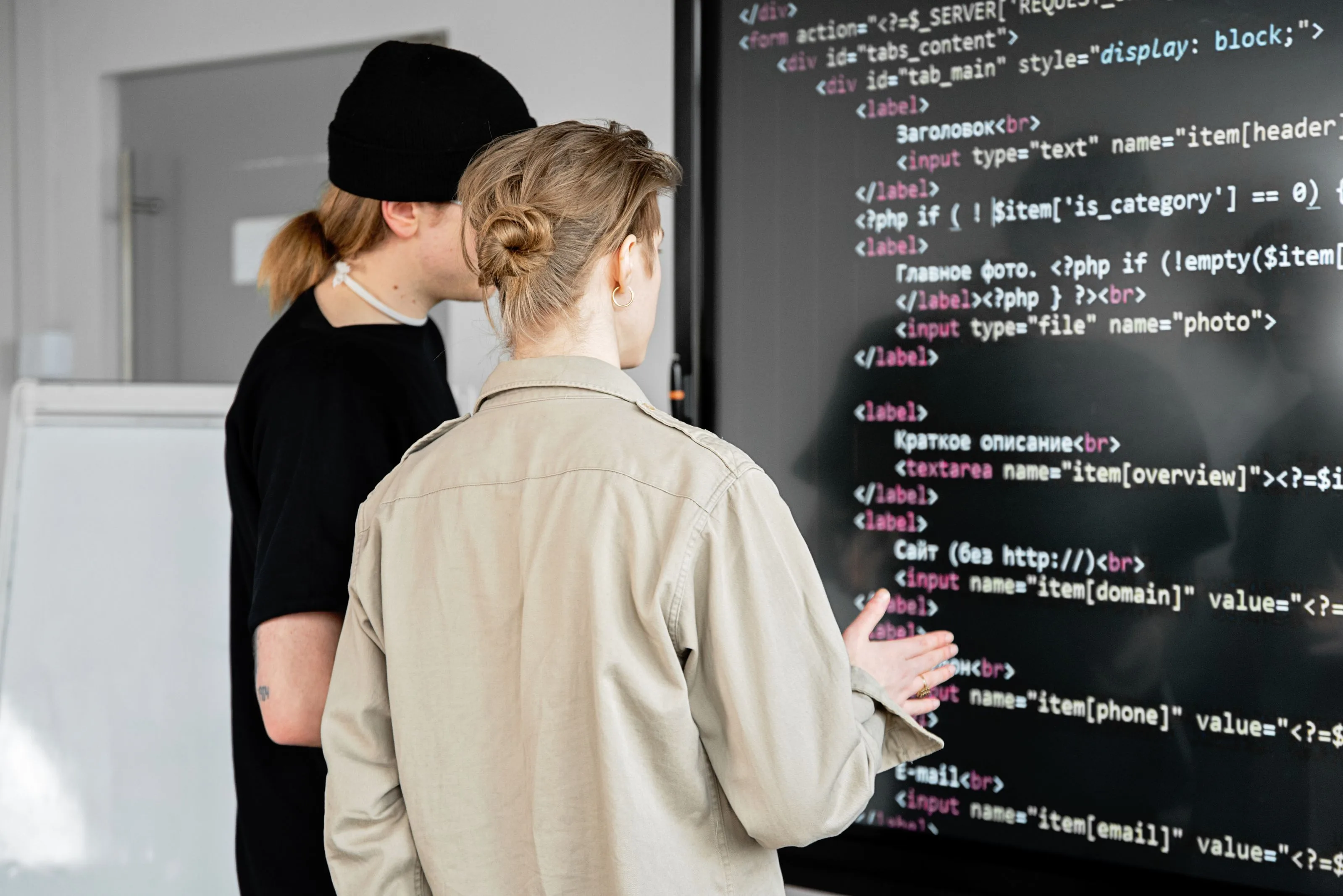 Two engineers reviewing source code on a large screen while planning a refactor