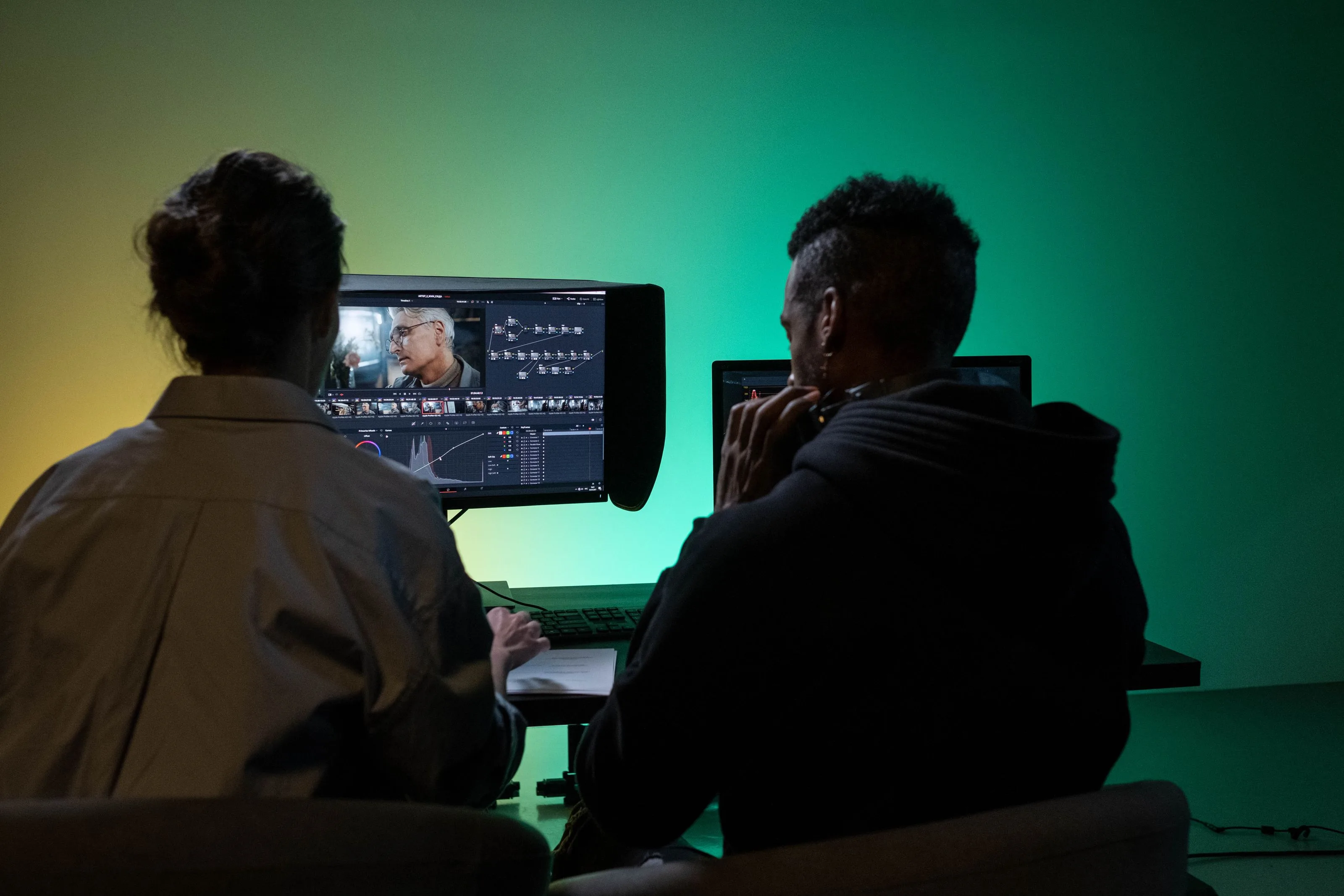Two editors reviewing a color grade on dual monitors with a node graph and scopes