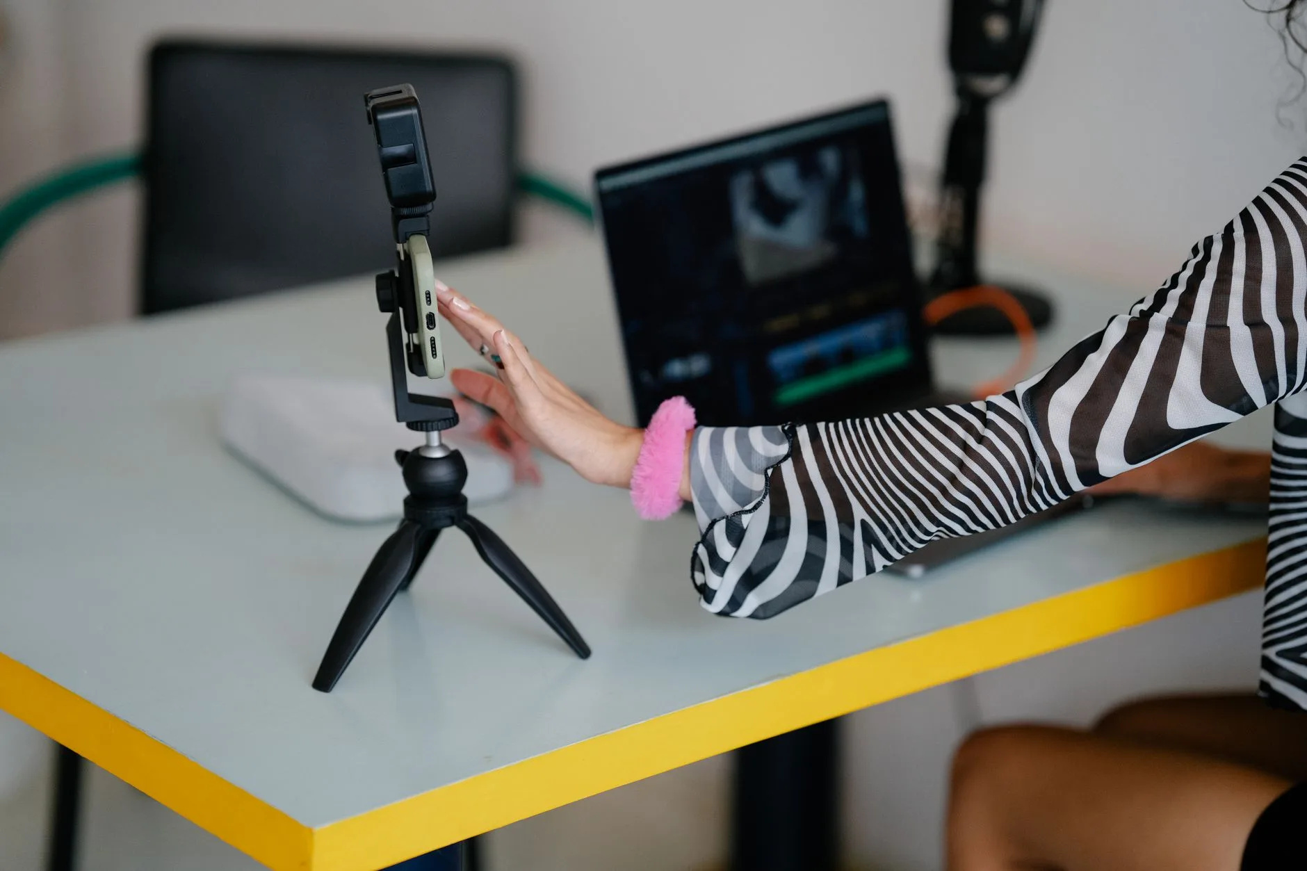 Woman adjusting a smartphone on a tripod with a laptop for video editing