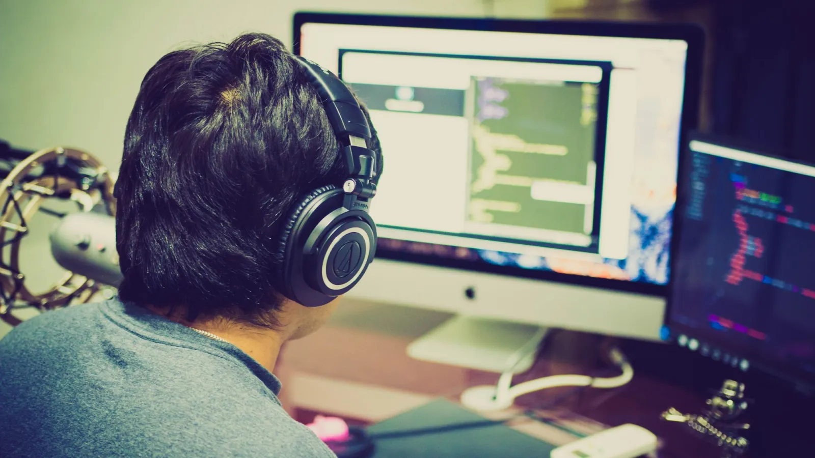 Programmer wearing headphones coding at a desk with dual monitors
