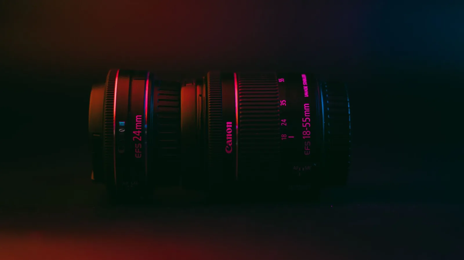 Moody close-up of Canon 24mm and 18-55mm lenses under vibrant lighting.