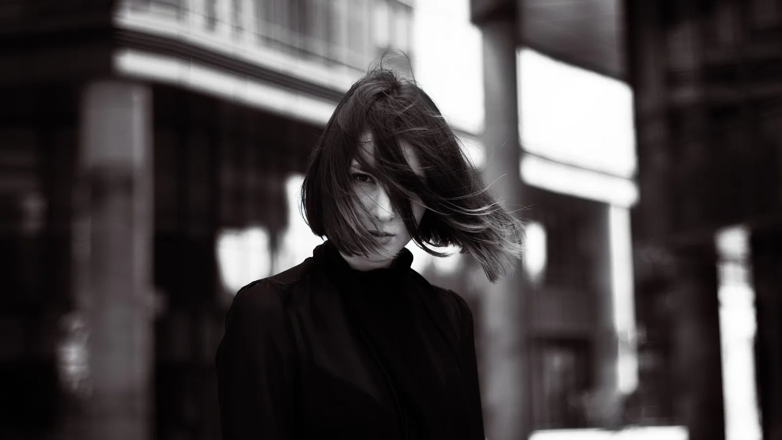 Black and white portrait of windblown hair against an urban backdrop, a low-contrast case needing manual touch-up