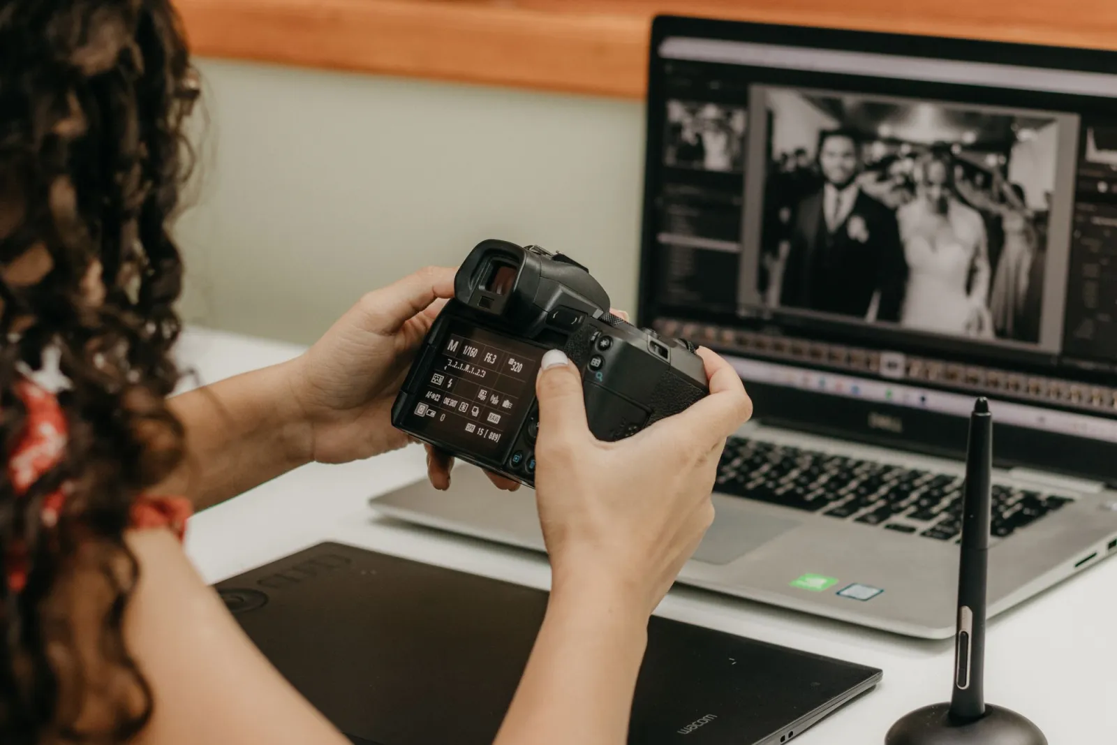 A photographer reviews and edits wedding photos on a laptop using a graphics tablet at her desk