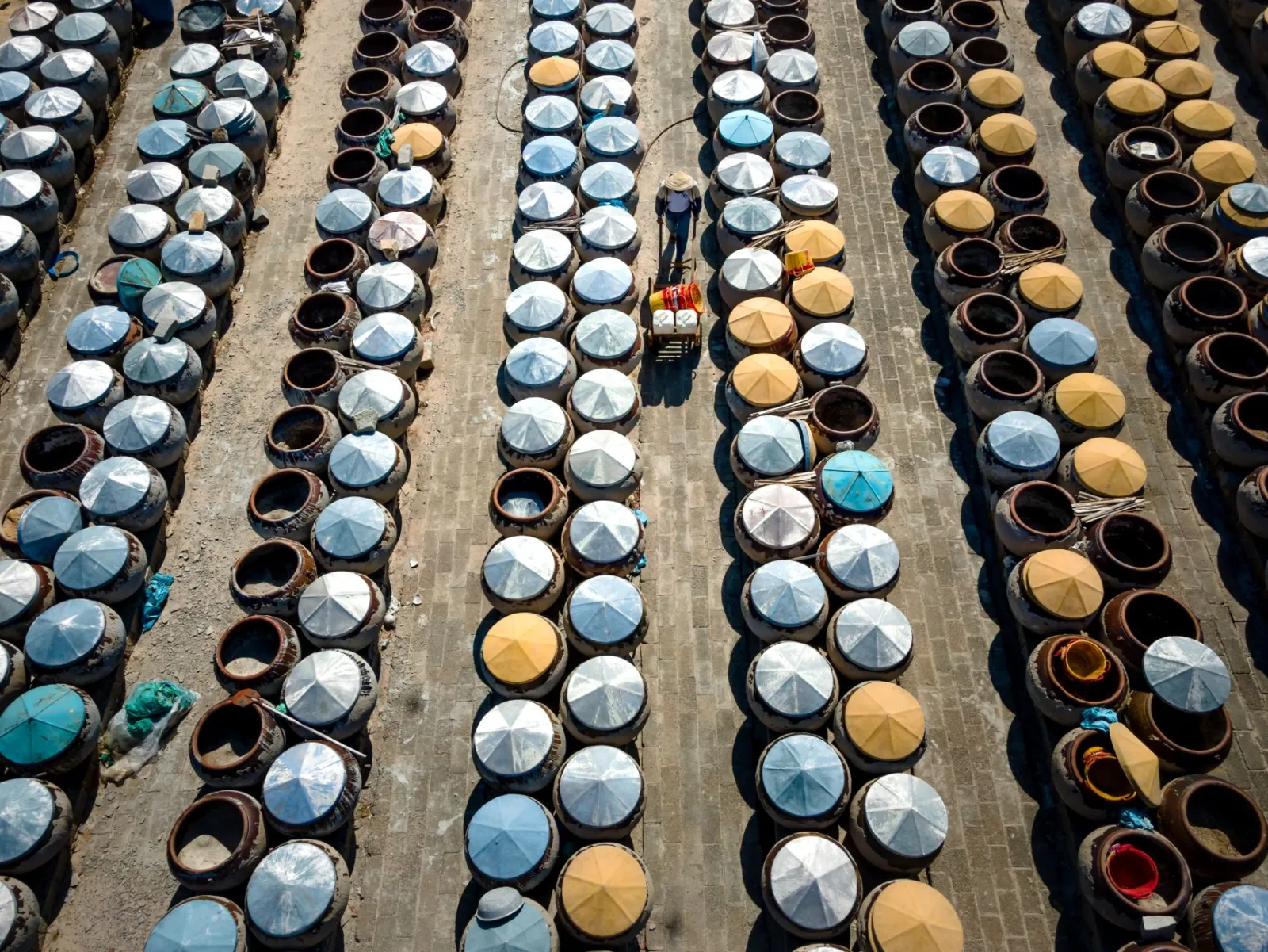 An aerial drone shot showing a person working among rows of fermentation containers outdoors.