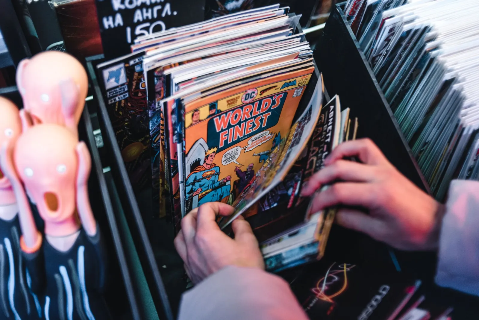 Hands browsing vintage comic books in a shop bin with bright cover art
