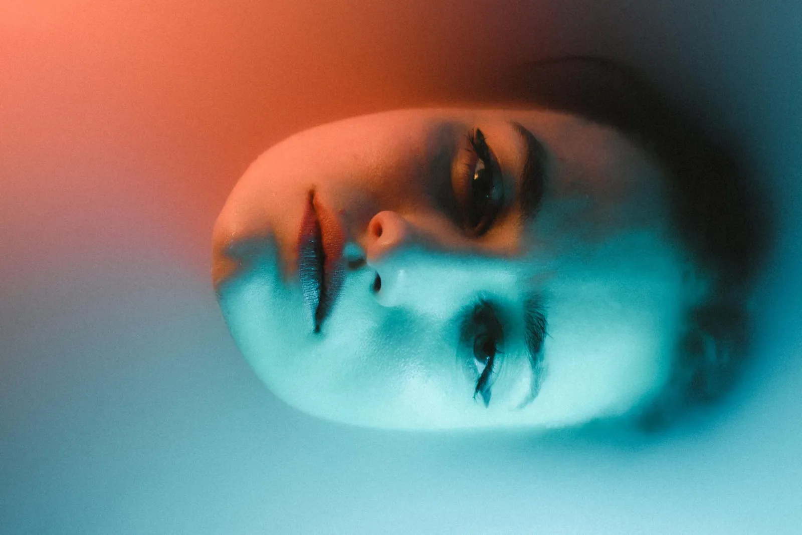 A captivating portrait of a woman's face submerged in water with dramatic red and blue lighting.