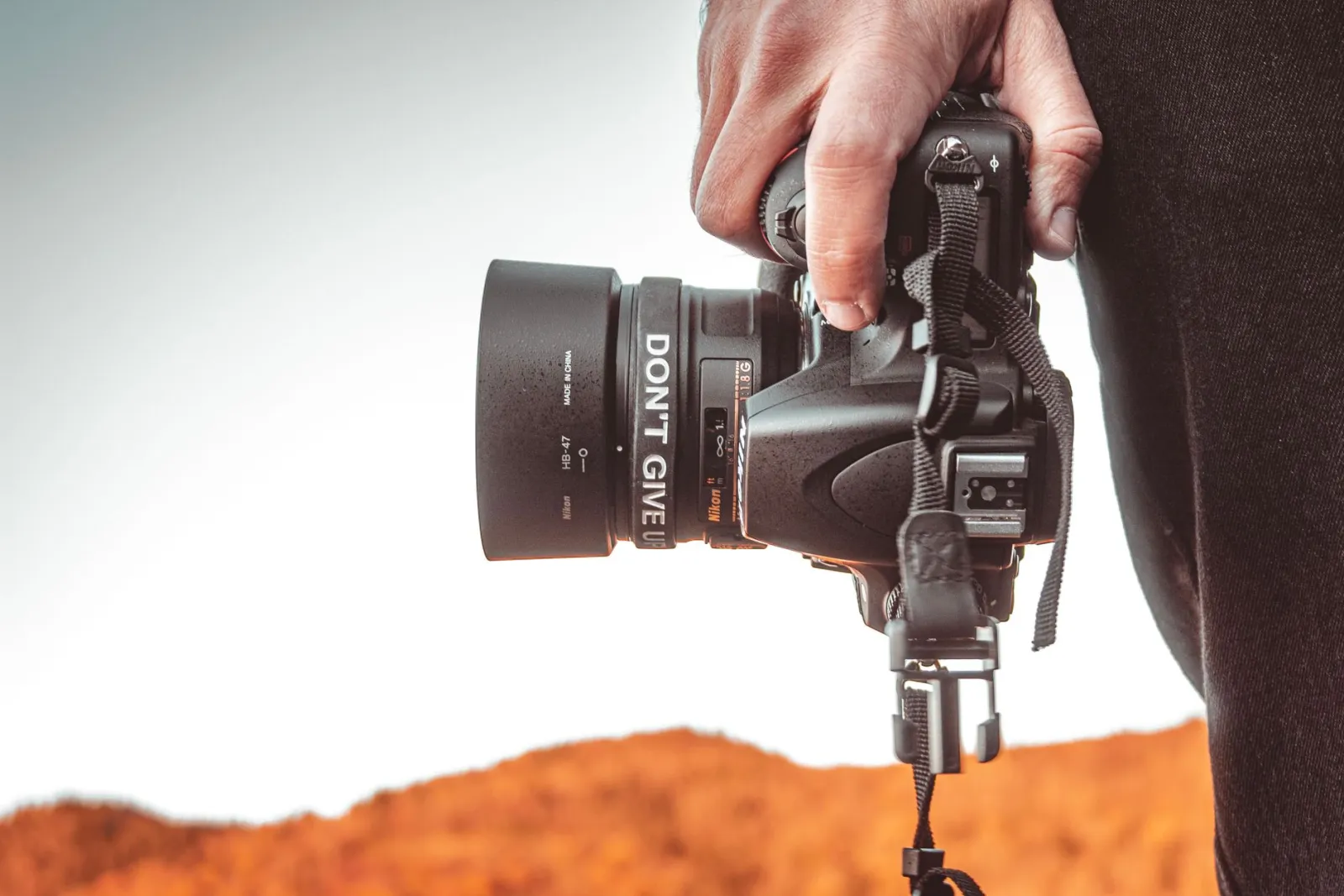 Photographer gripping a DSLR camera with motivational text outdoors.
