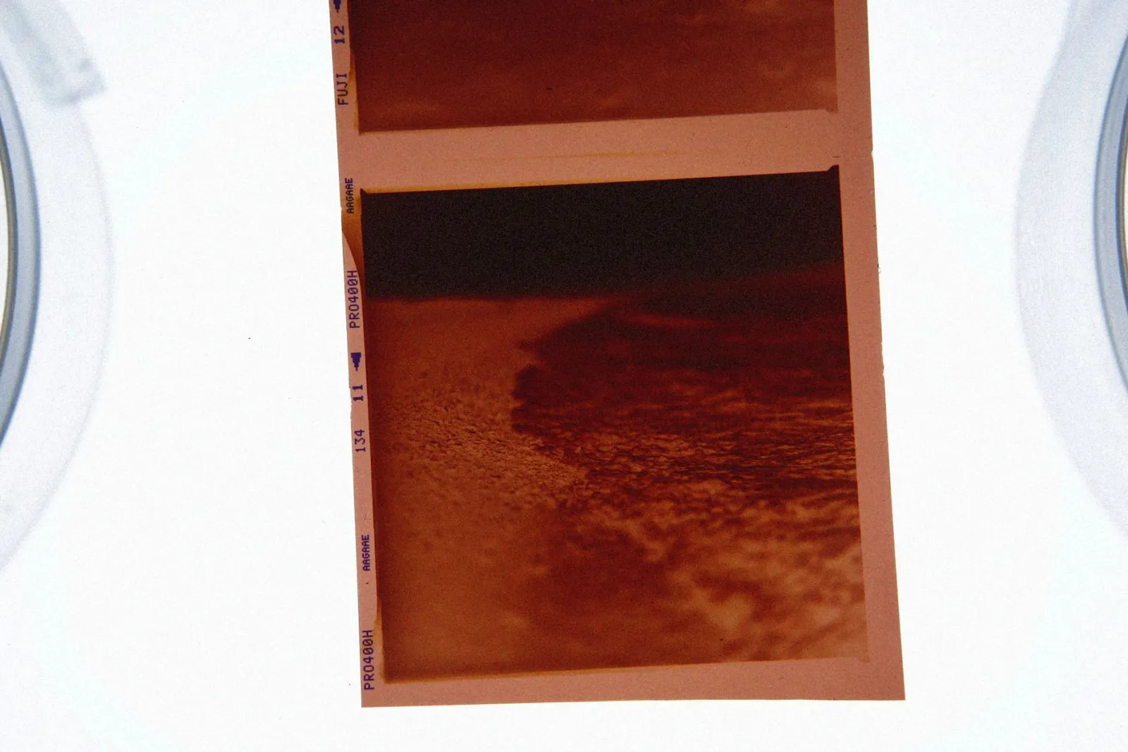 Film negative of a seacoast scene on lightbox, showcasing vintage photography style.