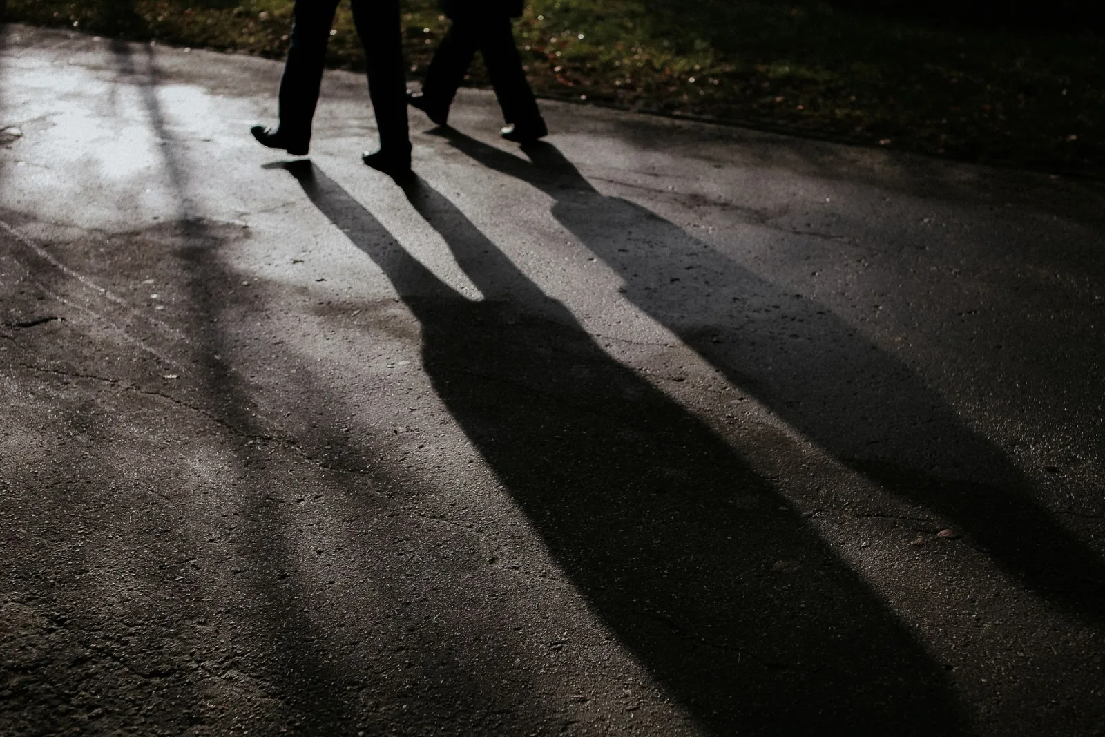 Two individuals walking on a wet road casting long shadows