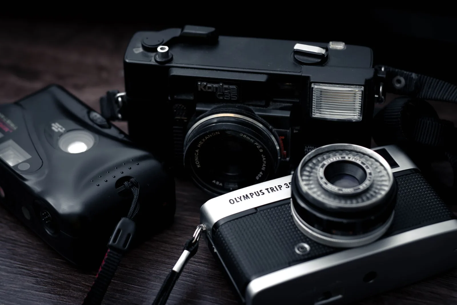 Analog film cameras including Olympus and Konica models resting on a wooden surface