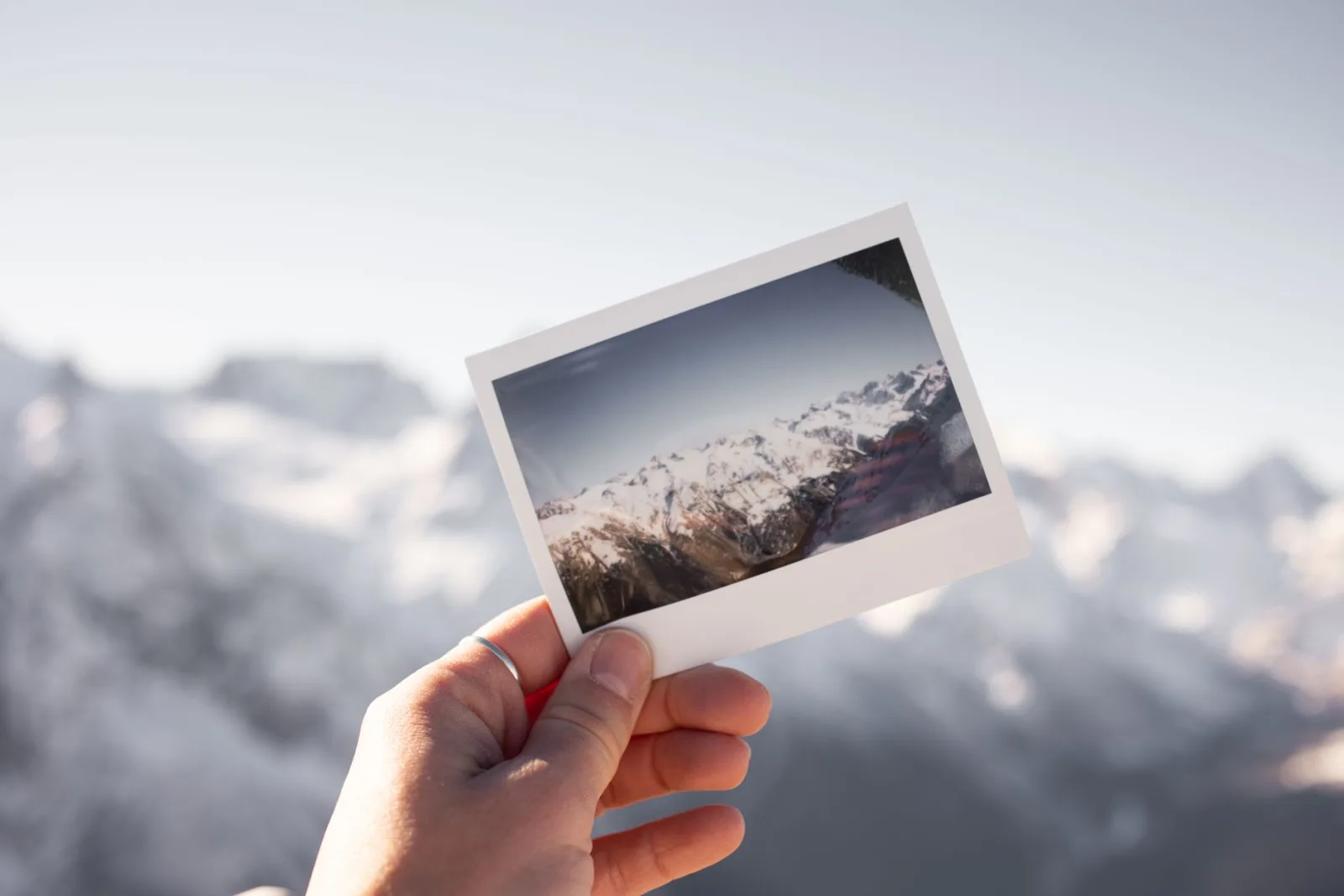 Hand holding a faded Polaroid photo of a snowy mountain landscape