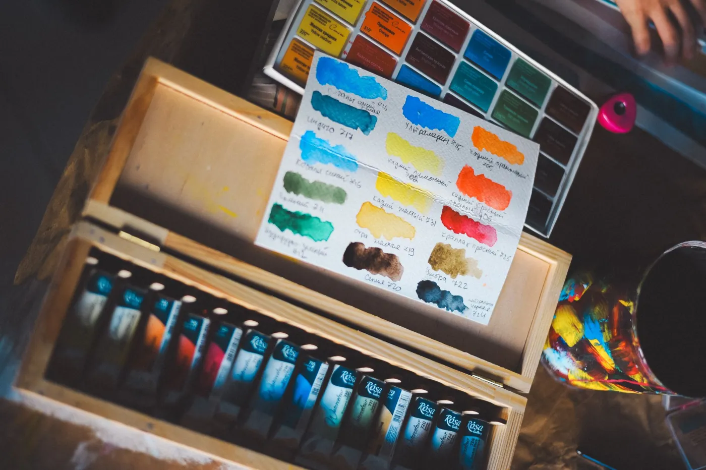 Watercolor paint swatches, brushes, and paper references on a desk for choosing texture and export style
