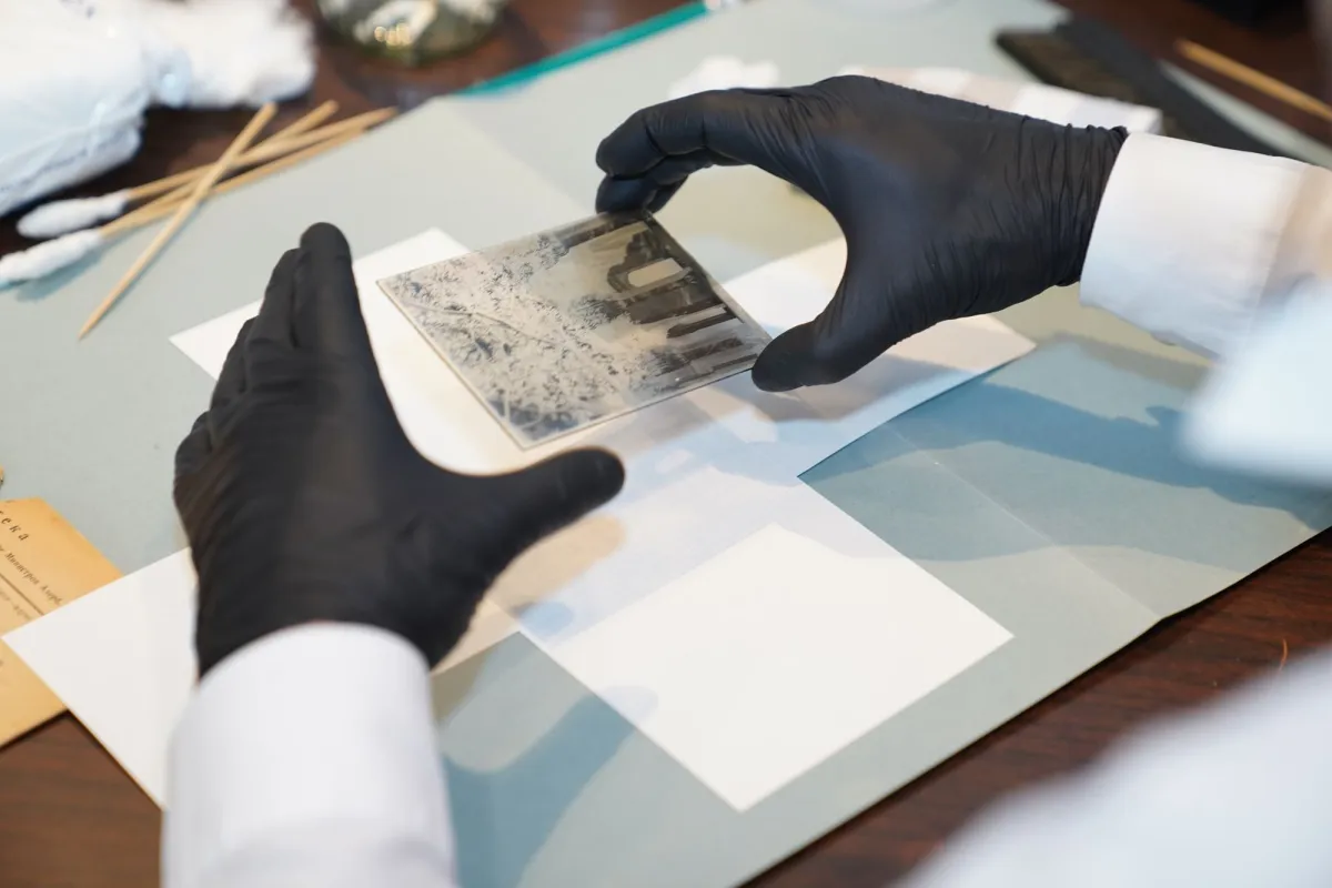 Gloved hands handling a glass-plate negative during archival photo restoration
