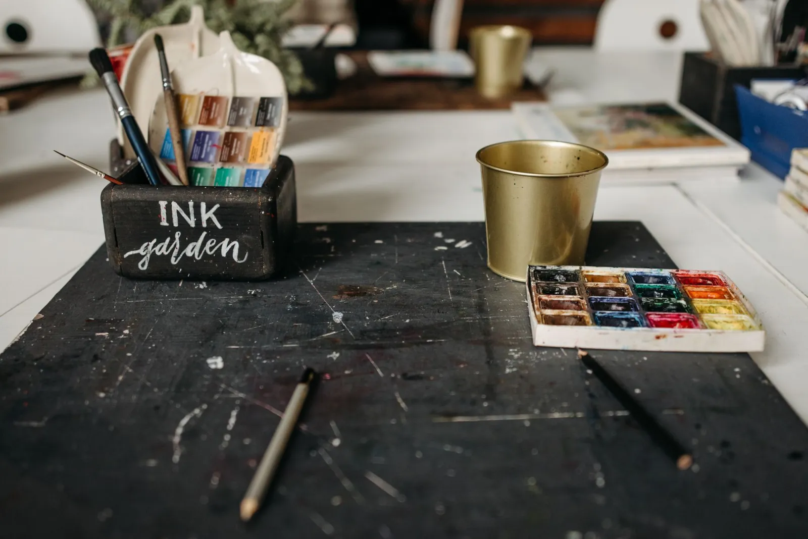 An art studio desk with brushes, watercolor pots, and supplies arranged in a creative workspace
