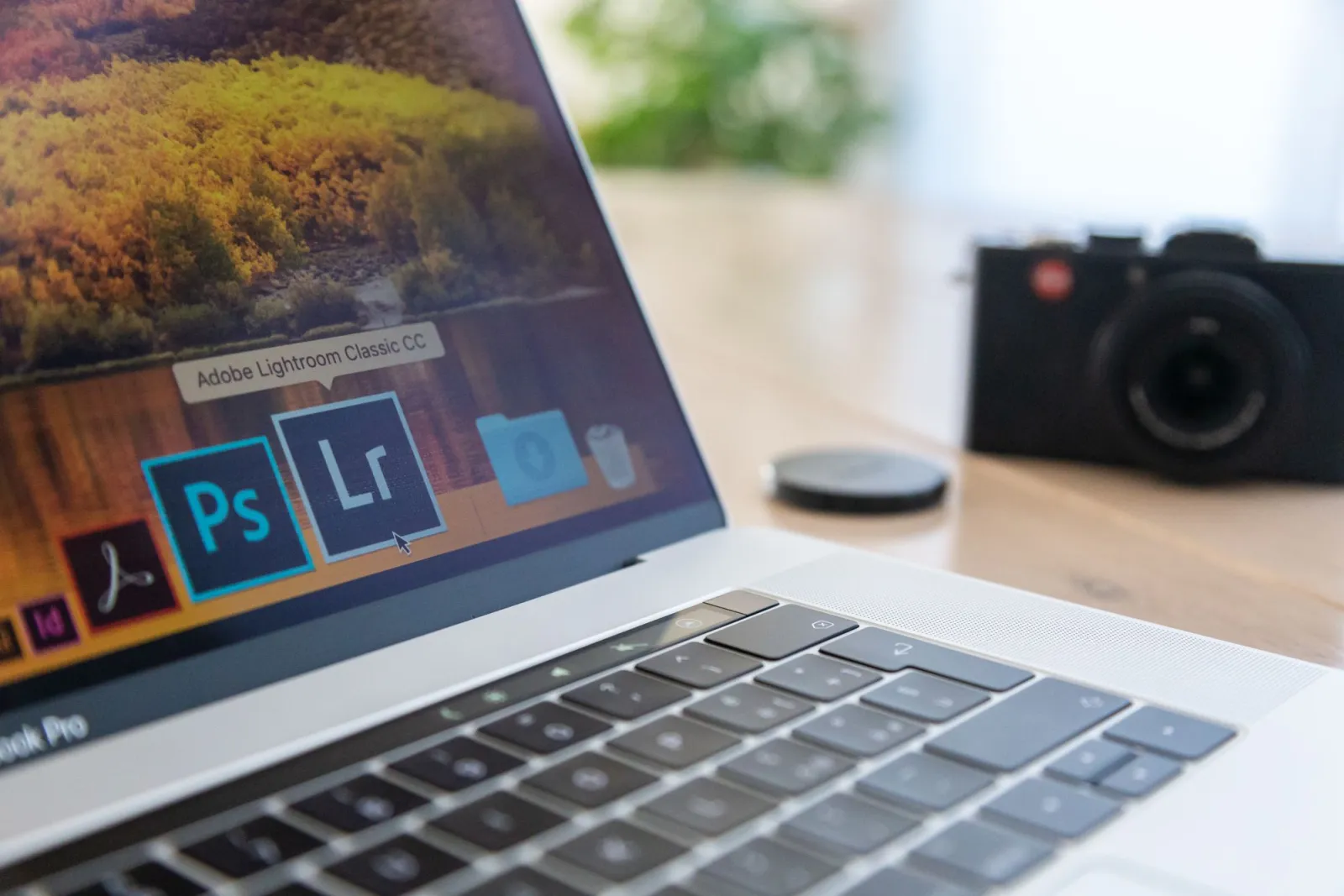 Laptop showing Adobe creative software icons next to a camera on a desk