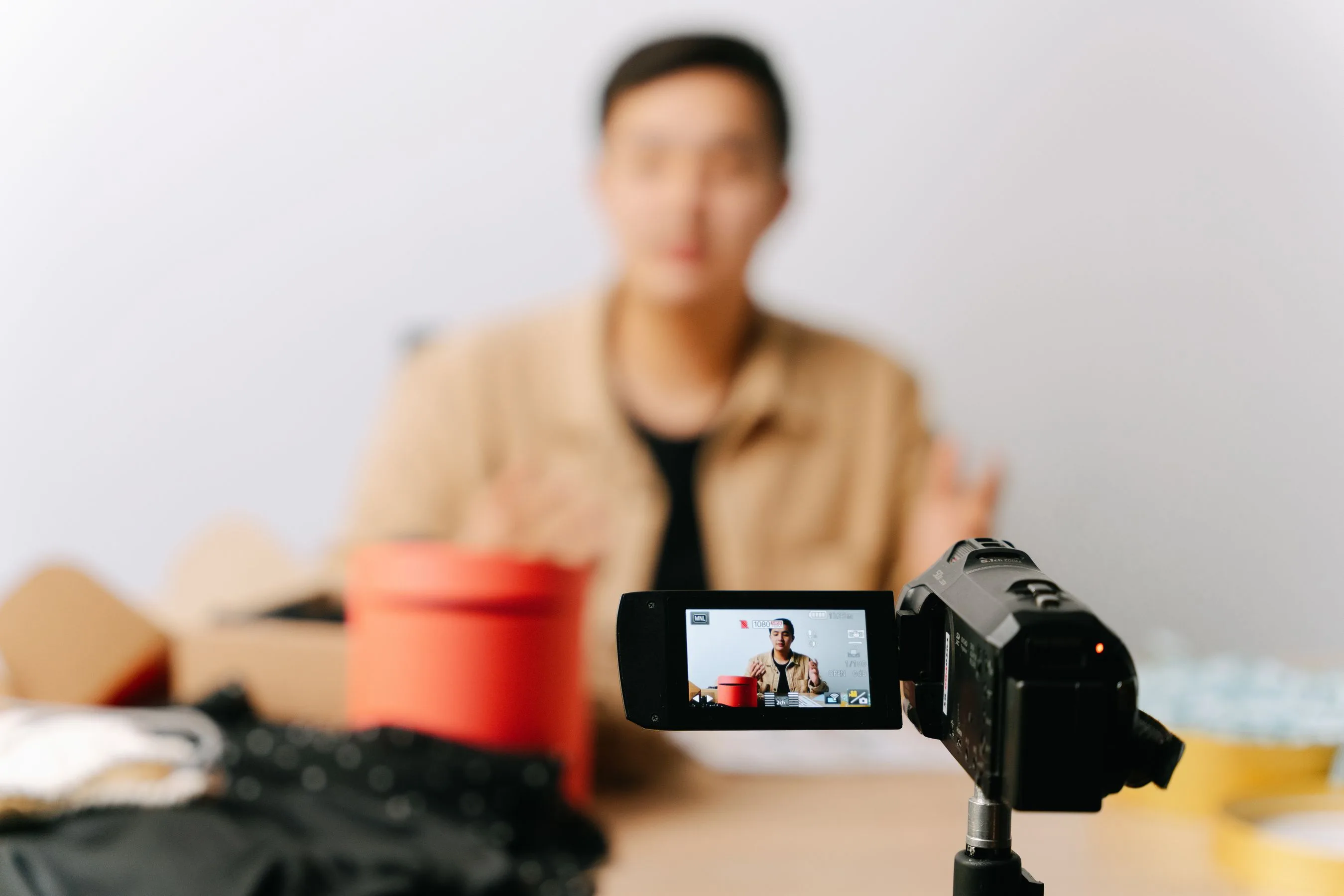 Creator filming a piece to camera on a camcorder, subject visible on the flip screen