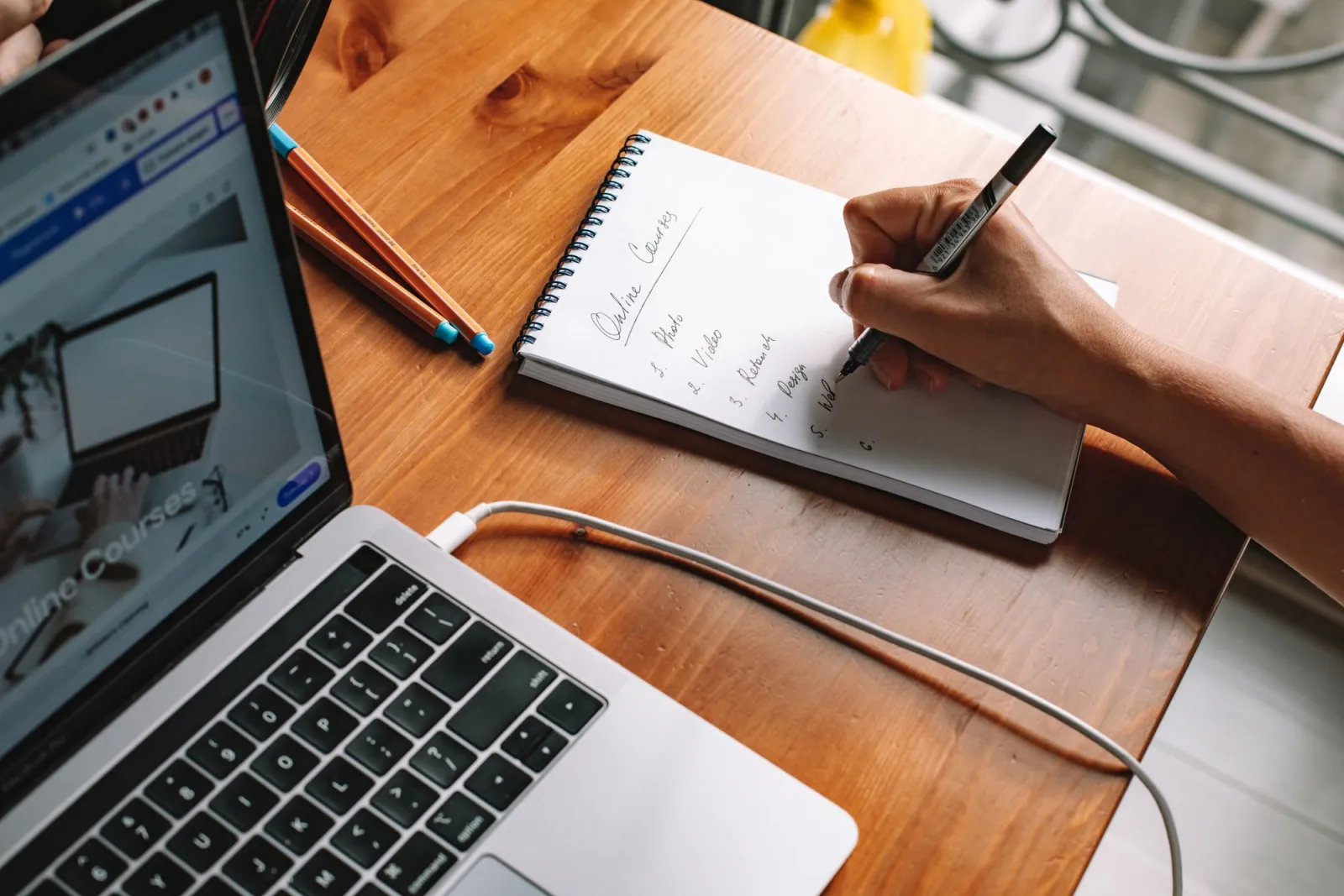 Person taking notes while watching online courses on a laptop at home